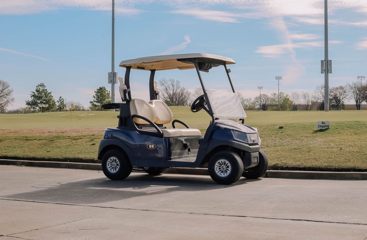 Home A golf cart parked on a pathway next to a golf course under a clear blue sky.