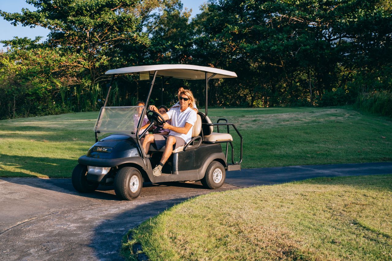 Home A family rides a golf cart on a sunny day in a lush golf course setting.